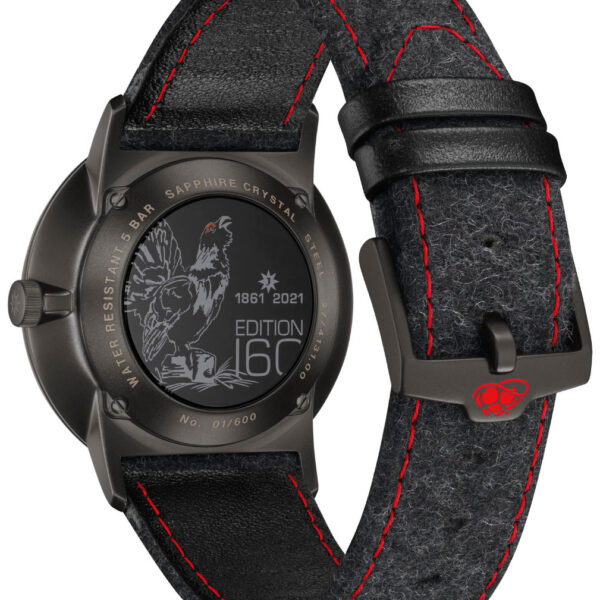 Die Rückseite der Uhr Junghans Form A Edition 160 zeigt eine Hahngravur, „1861 2021“ und „Edition 160“. Sie hat ein schwarzes Lederarmband mit roten Nähten, eine Metallschließe, ein rotes Logo und ist als limitierte Auflage „01/600“ gekennzeichnet.