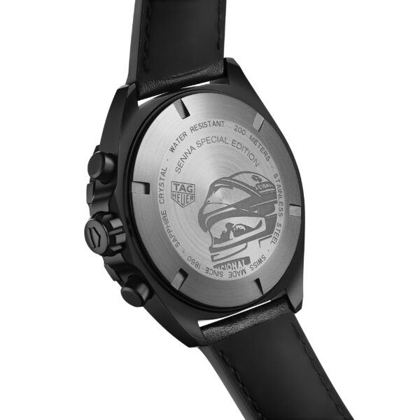 Das Bild zeigt die Rückseite einer Tag Heuer-Uhr mit schwarzem Lederarmband. Auf der Rückseite ist ein Rennhelm eingraviert und es sind Inschriften zu sehen, die darauf hinweisen, dass es sich um eine „Senna Special Edition“ handelt. Außerdem sind Angaben zur Wasserdichtigkeit und Modelldetails zu sehen.