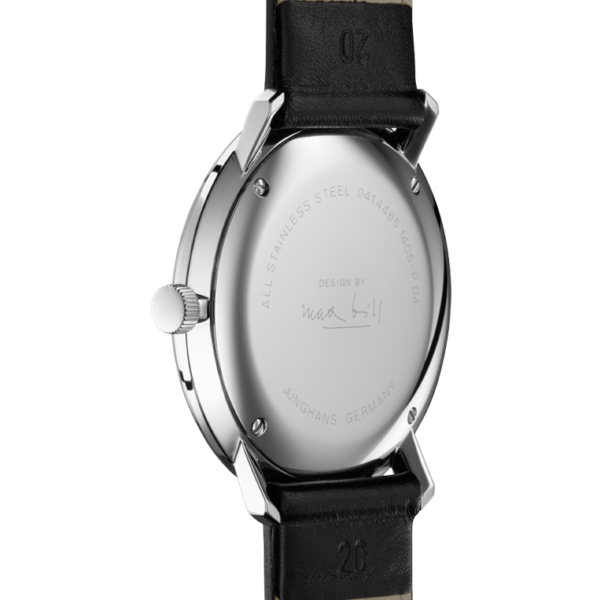Das Bild zeigt die Rückseite einer Junghans Max Bill Quarz-Armbanduhr mit Edelstahlgehäuse und schwarzem Lederarmband. Auf der Rückseite ist neben einer unleserlichen Signatur „DESIGN BY“ eingraviert, mit einer Krone auf der linken Seite und zusätzlich eingraviertem Text.