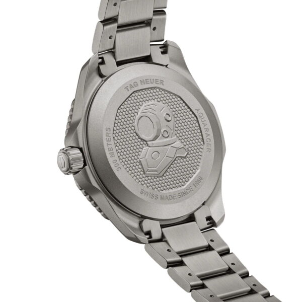 Das Bild zeigt die Rückseite einer silbernen Tag Heuer Aquaracer-Uhr mit einem eingravierten Bild eines Taucherhelms. Der Text weist auf eine Wasserdichtigkeit bis 300 Meter hin und weist darauf hin, dass die Uhr in der Schweiz hergestellt wurde. Das Metallarmband ist teilweise sichtbar.