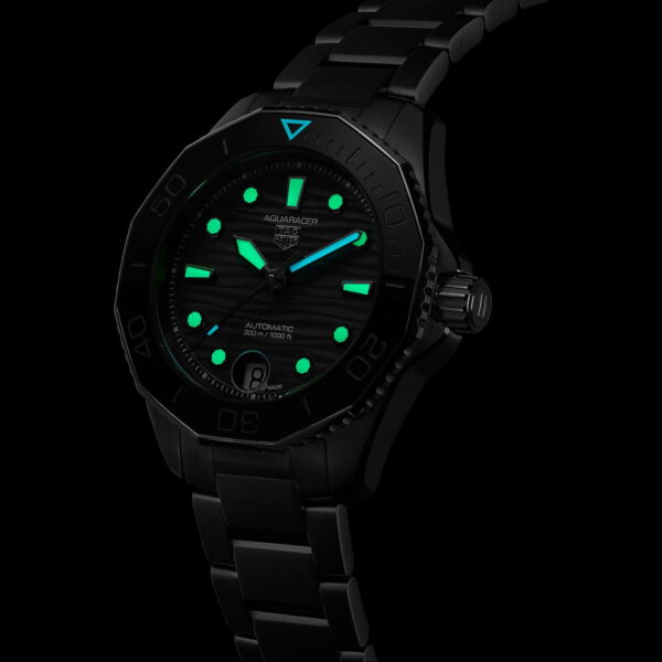 Eine schwarze Taucheruhr mit Metallarmband ist in dunkler Umgebung abgebildet. Das Zifferblatt verfügt über leuchtend grüne Indizes und Zeiger, wobei eine dreieckige Markierung bei der 12-Uhr-Position hell leuchtet.