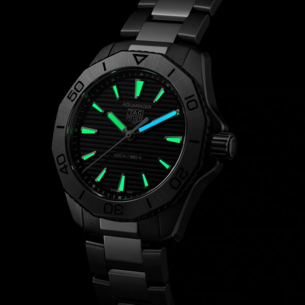 Eine schwarze TAG Heuer Aquaracer-Uhr mit leuchtend grünen Zeigern und Markierungen auf dunklem Hintergrund. Die Uhr hat ein Edelstahlarmband und ein sichtbares „Aquaracer“-Logo auf dem Zifferblatt.