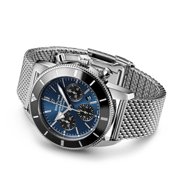 Eine luxuriöse Breitling-Uhr mit blauem Zifferblatt und drei Hilfszifferblättern sowie silbernen Stundenmarkierungen und Zeigern. Sie hat eine schwarze Lünette und ein Edelstahl-Netzarmband, das schräg angebracht ist, um das Design hervorzuheben.