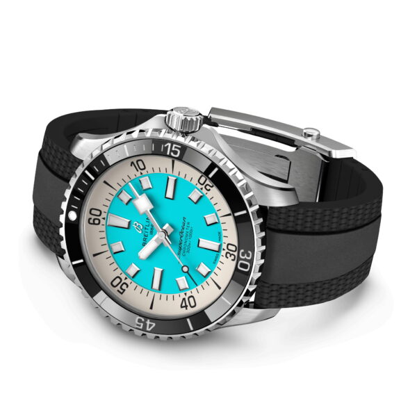 Eine luxuriöse Armbanduhr mit türkisfarbenem Zifferblatt, auffälligen weißen Stundenmarkierungen und schwarzem Gummiarmband. Die Lünette aus Edelstahl hat Minutenmarkierungen und einen strukturierten Rand. Das Armband hat ein gemustertes Detail und einen Metallverschluss.