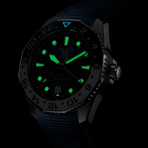 Eine Uhr mit dunklem Zifferblatt und leuchtend grünen Markierungen. Die Lünette hat Zahlen und die Zeiger sind teilweise sichtbar. Das Armband scheint aus Gummi zu sein. Das Zifferblatt ist vor einem dunklen Hintergrund deutlich beleuchtet.
