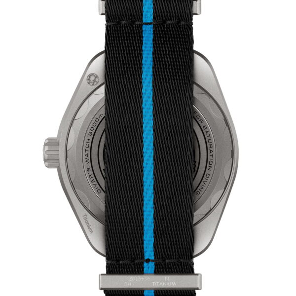 Das Bild zeigt die Rückseite einer Uhr mit schwarzem Armband mit einem blauen Mittelstreifen. Auf der metallischen Rückseite der Uhr sind ein Text und ein kleines Logo eingraviert. Oben und unten sind die Schnalle und die Armbandschlaufen sichtbar.