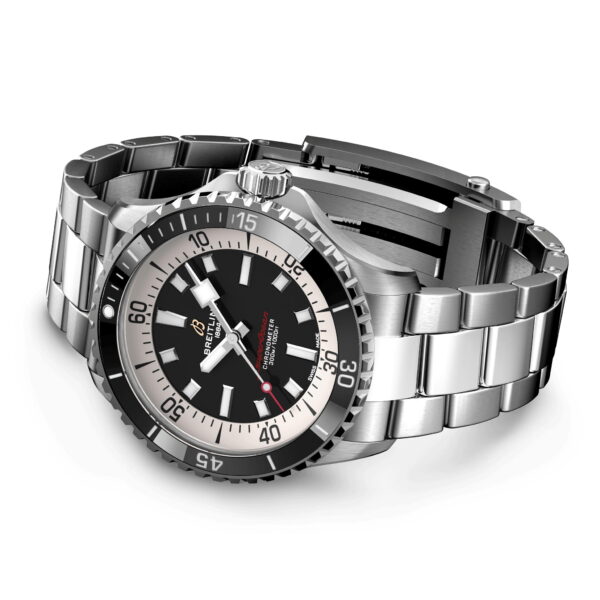 Eine silberne Armbanduhr mit Metallarmband, schwarzem Zifferblatt, großen weißen Stundenmarkierungen und drehbarer Lünette mit Ziffern. Die Zeiger sind markant und das Markenlogo ist auf dem Zifferblatt sichtbar.