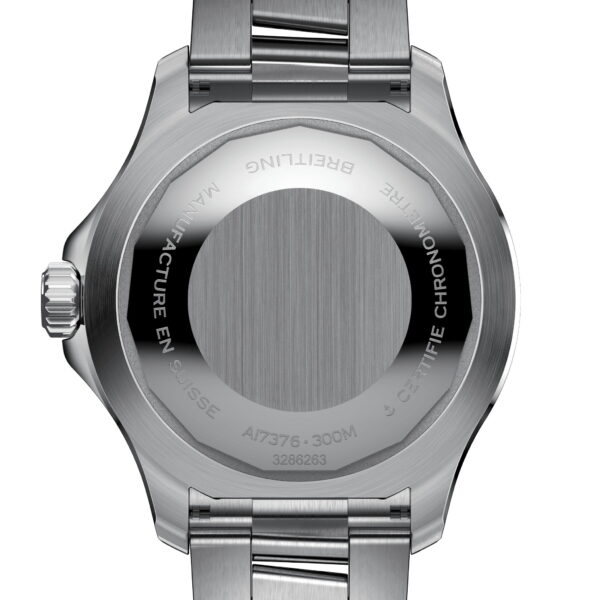 Das Bild zeigt die Rückseite einer silbernen Metallarmbanduhr, auf deren runder Oberfläche deutlich eingravierter Text zu sehen ist. Die Uhr hat eine gebürstete Metalloberfläche, eine verschraubte Krone an der Seite und ein Metallarmband mit Gliedern.