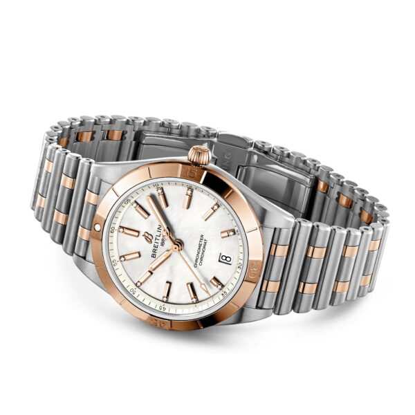 Eine luxuriöse Armbanduhr mit einem silbernen und goldenen Metallarmband. Die Uhr hat ein perlweißes Zifferblatt sowie goldene Stundenmarkierungen und Zeiger. Sie verfügt über eine Datumsanzeige bei 3 Uhr und das Markenlogo bei 12 Uhr. Das Gehäuse kombiniert Gold- und Silbertöne.