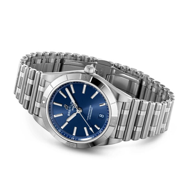 Eine silberne Edelstahluhr mit blauem Zifferblatt und silbernen Stundenmarkierungen. Sie verfügt über ein Datumsfenster auf der 3-Uhr-Position und hat ein Gliederarmband aus Metall. Die Uhr wird schräg gezeigt, was ihr schlankes Design hervorhebt.