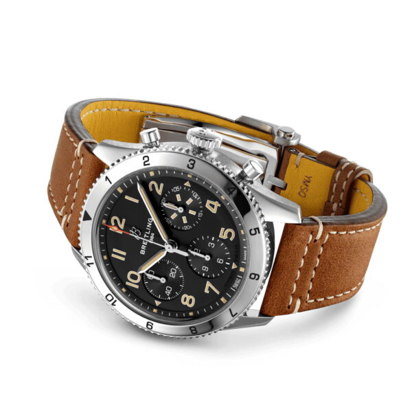 Der Breitling Classic AVI Chronograph 42 P51-Mustang ist eine Luxusuhr mit braunem Lederarmband, silberner Lünette und silbernem Verschluss. Das schwarze Zifferblatt zeigt mehrere Zifferblätter und goldene Ziffern sowie den Markennamen.