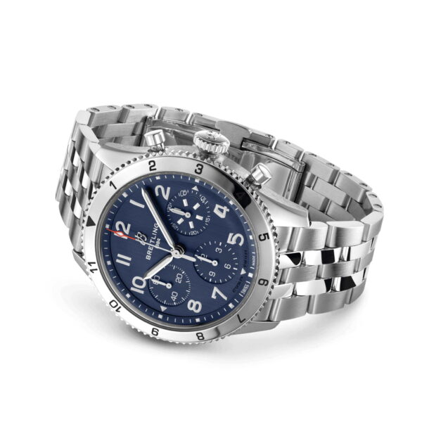Der Breitling Classic AVI Chronograph 42 ist eine Luxusuhr mit Edelstahlgehäuse, blauem Zifferblatt mit kräftigen weißen Ziffern, drei Hilfszifferblättern und einer Lünette mit Minutenmarkierungen. Er verfügt über ein silbernes Metallarmband und eine polierte Oberfläche und verkörpert Eleganz und Präzision.