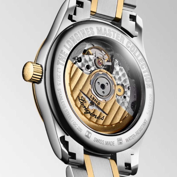Nahaufnahme der Rückseite einer Luxusuhr, die ihr kompliziertes mechanisches Uhrwerk zeigt. Das Gehäuse ist silberfarben mit goldenen Akzenten. Der eingravierte Text erwähnt „The Longines Master Collection“ und enthält Details wie „Automatisch“ und „Wasserfest“.