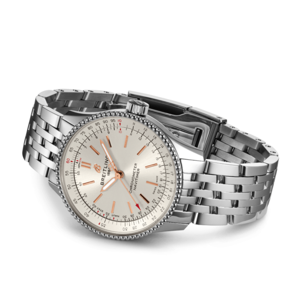 Der Breitling Navitimer 1 Automatic 35 verfügt über ein silbernes Zifferblatt, eine detaillierte Lünette, rote Stundenmarkierungen, eine Datumsanzeige und einen Markennamen auf dem Zifferblatt. Er hat ein Metallarmband mit Gliedern und ist leicht nach rechts geneigt.