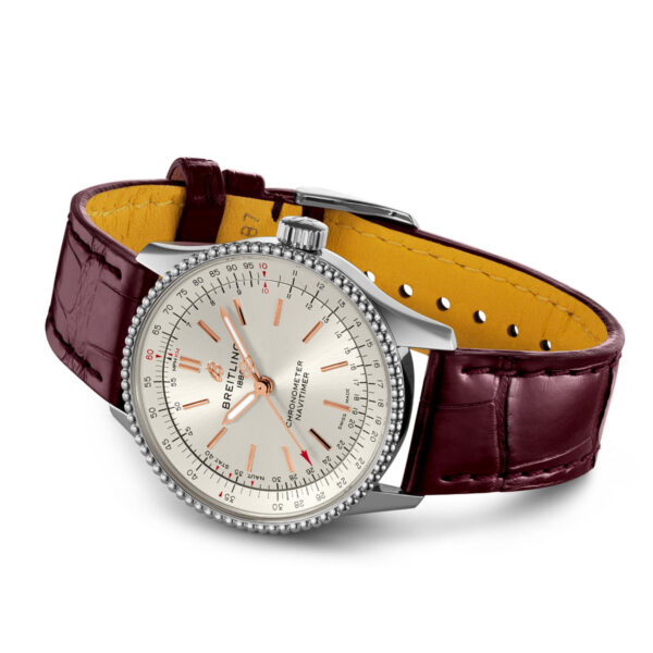 Die Breitling Navitimer 1 Automatic 35 verfügt über ein rundes, silbernes Zifferblatt mit roten und schwarzen Markierungen, die mit dem Markennamen verziert sind. Sie ist mit einem dunkelbraunen Lederarmband mit kontrastierender gelber Innenseite gepaart.