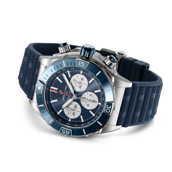 Die Breitling Super Chronomat B01 44 ist eine Luxusarmbanduhr mit blauem Zifferblatt und Lünette, drei Hilfszifferblättern und leuchtenden Stundenmarkierungen. Sie hat ein strukturiertes blaues Armband, ein Edelstahlgehäuse mit Drückern und Krone und ihre Lünette ist mit Zahlen und Indizes verziert.