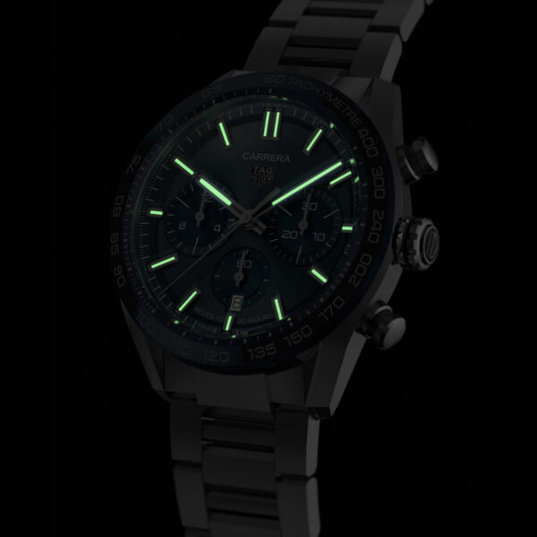 Der TAG Heuer Carrera Chronograph verfügt über ein dunkles Design mit einem Metallarmband, leuchtend grünen Zeigern und Markierungen auf schwarzem Hintergrund, wodurch seine leuchtenden Eigenschaften hervorgehoben werden.