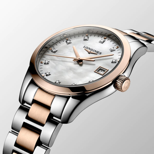 Die Luxusarmbanduhr Longines Conquest Classic verfügt über ein silber- und goldfarbenes Metallarmband. Das Perlmuttzifferblatt verfügt über Diamant-Stundenmarkierungen, eine Datumsanzeige und zeigt den Markennamen und das Logo auf einem hellgrauen Hintergrund.