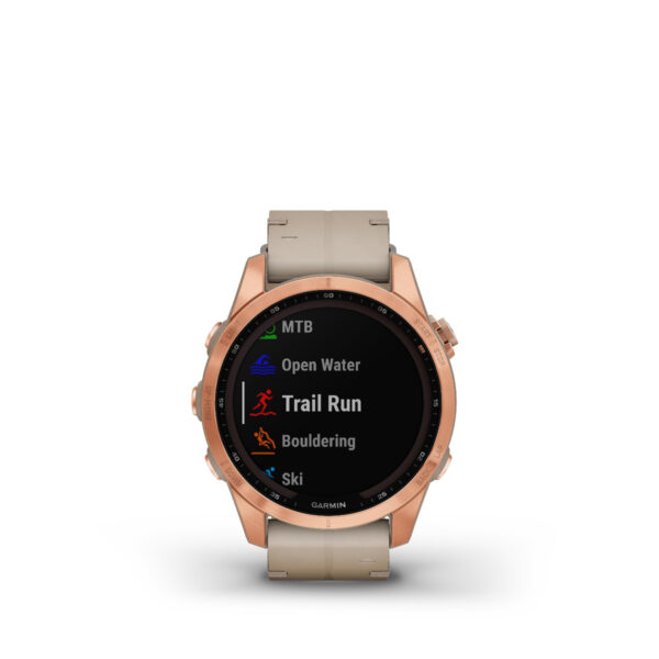 Die Garmin Fenix 7S Sapphire Solar Edition mit roségoldener Lünette und rundem Zifferblatt sowie beigem Armband zeigt Menüoptionen wie MTB, Open Water, Trail Run, Bouldern und Ski an.