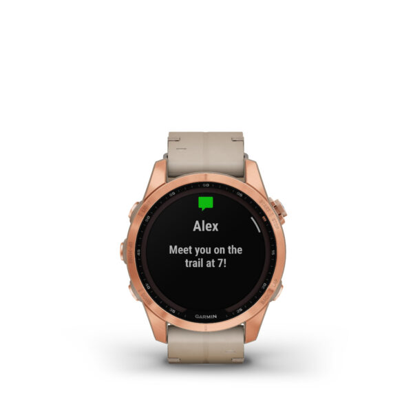 Die Garmin Fenix 7S Sapphire Solar Edition mit roségoldener Lünette, beigem Armband und schwarzem Bildschirm zeigt eine Nachricht von Alex an: „Wir treffen uns um 7 auf dem Trail!“.