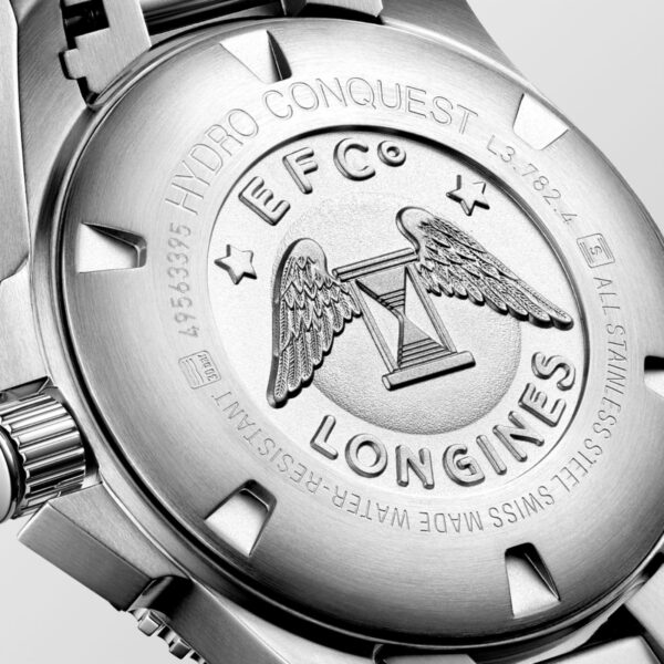 Nahaufnahme einer silbernen Uhrengehäuserückseite, in die das Longines-Logo mit Flügeln und einer Sanduhr eingraviert ist. Der umgebende Text enthält „EFC“ und „HYDRO CONQUEST“ und hebt die Handwerkskunst und Identität der Longines HydroConquest hervor.
