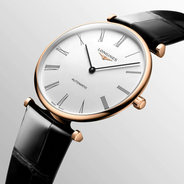 Die Longines La Grande Classique de Longines ist eine elegante Armbanduhr mit weißem Zifferblatt, goldenem Gehäuse und schwarzem Lederarmband. Sie hat römische Ziffern und dünne schwarze Zeiger, mit dem Markennamen und „Automatic“ auf dem Zifferblatt, vor einem schlichten hellen Hintergrund.