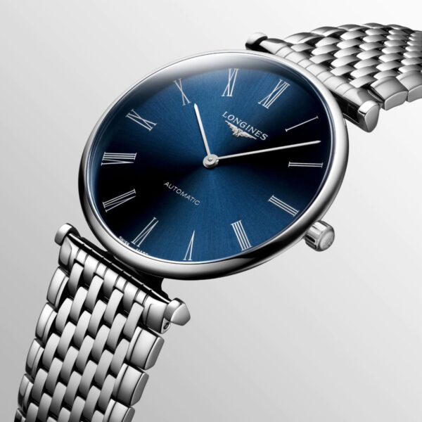 Die Longines La Grande Classique zeichnet sich durch ein elegantes Design mit silbernem Metallarmband und rundem blauem Zifferblatt aus. Sie zeigt römische Stundenmarkierungen und schlanke silberne Zeiger auf einem eleganten hellgrauen Hintergrund.