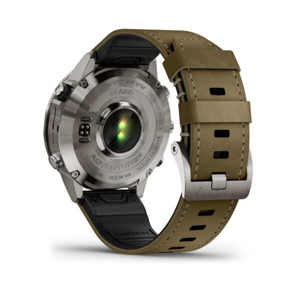 Das Bild zeigt die Rückseite einer Garmin Marq Adventurer 2.Gen. Smartwatch mit rundem Metallgehäuse und braunem Lederarmband, mit grünem Sensor und Textgravuren. Im Fokus stehen die Schnalle und ein Teil des Armbands.