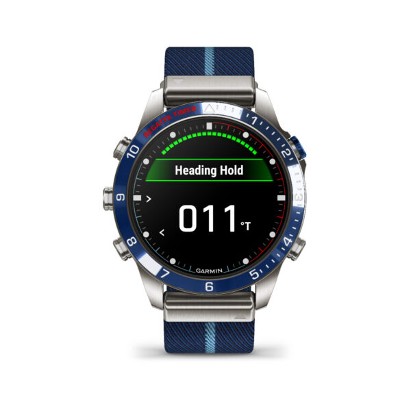 Die Smartwatch Garmin Marq Captain 2.Gen. verfügt über eine blaue Lünette mit der Anzeige „Heading Hold“ und „011°“, ein blau-schwarz gestreiftes Stoffarmband mit Metalldetails und ein Kompassdesign auf dem Zifferblatt mit Zahlen am Rand.