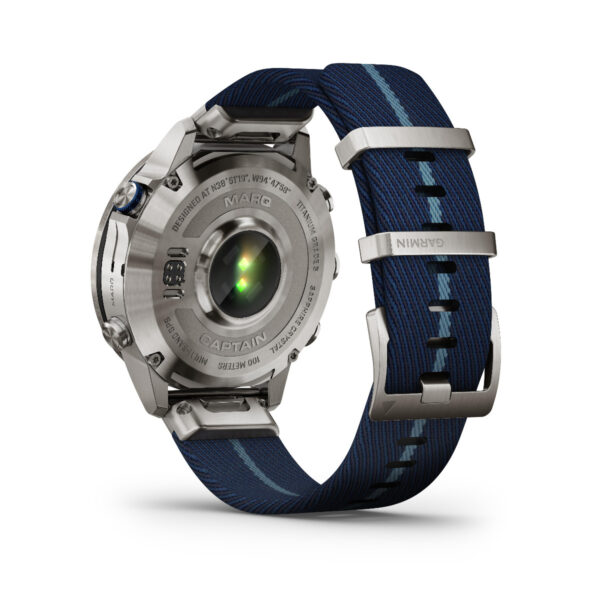 Rückansicht des Garmin Marq Captain 2.Gen., das sein luxuriöses Metallgehäuse mit eingraviertem Text und einem grünen Sensor zeigt, ergänzt durch ein blau gestreiftes Band. Das Armband umfasst Metallanschlüsse und einen Markenverschluss.