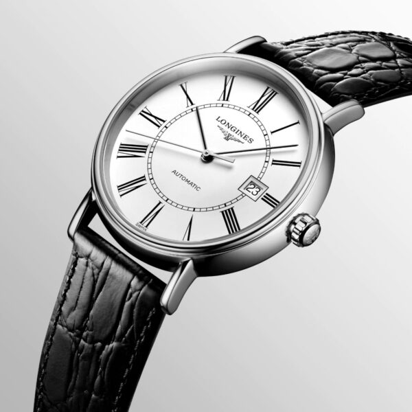 Die Longines Présence Automatic verfügt über ein weißes Zifferblatt mit schwarzen römischen Ziffern und ein schwarzes Lederarmband. Auf dem Zifferblatt stehen „Longines“ und „Automatic“, das Datum wird bei drei Uhr angezeigt. Der Hintergrund ist ein sanfter Grauverlauf.
