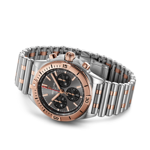 Der Breitling Chronomat B01 Chronograph 42 ist eine Luxusarmbanduhr mit einem silber- und roségoldfarbenen Edelstahlarmband und -gehäuse. Sie hat ein schwarzes Zifferblatt mit drei Hilfszifferblättern, eine Datumsfunktion und roségoldfarbene Akzente, darunter die Lünette, die Krone und die Stundenmarkierungen.