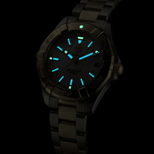 Die TAG Heuer Aquaracer verfügt über ein dunkles Metallband und leuchtend blaue Markierungen und Zeiger, die bei schwachem Licht sichtbar sind. Auf dem dunklen Zifferblatt sind dezente Markenzeichen und Ziffern zu sehen, die durch das Licht erhellt werden.