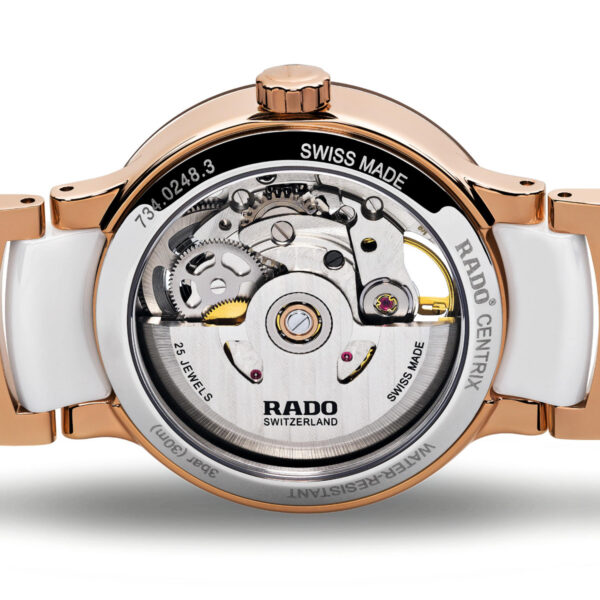 Eine Nahaufnahme der Armbanduhr Rado Centrix Autom. Diamonds Open Heart zeigt ihr Innenleben. Sie verfügt über ein Gehäuse aus Roségold und Weiß mit sichtbaren Zahnrädern. Auf den komplizierten Komponenten sind deutlich „Rado“, „Swiss Made“ und „25 Jewels“ zu sehen.