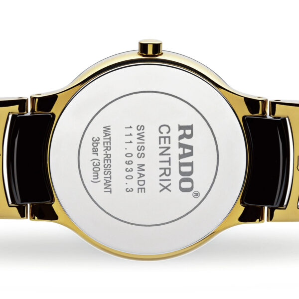 Eine Nahaufnahme der Rückseite der Rado Centrix zeigt ein goldenes und schwarzes Band. Auf der silbernen Rückseite ist „RADO CENTRIX SWISS MADE“ eingraviert, einschließlich Angaben zur Wasserbeständigkeit und zum Modell.