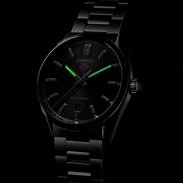 Vor einem dunklen Hintergrund ist eine TAG Heuer Carrera-Armbanduhr mit einem eleganten schwarzen Metallarmband zu sehen. Sie verfügt über leuchtend grüne Zeiger und Stundenmarkierungen, auf dem Zifferblatt ist das Markenlogo sichtbar.