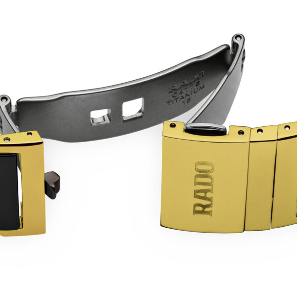 Eine Nahaufnahme eines Rado Integral Diamonds-Uhrenarmbands zeigt ein goldenes und schwarzes Gliederdesign. In der teilweise geöffneten Schließe sind „Rado“, „Titanium“ und mehrere Zahlen eingraviert, die das Material und die Marke angeben.