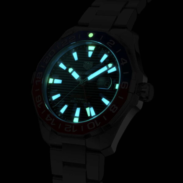 Die TAG Heuer Aquaracer Cal. 7 GMT mit Edelstahlarmband und nummerierter Drehlünette besticht im Dunkeln durch ihr leuchtend blau-weißes Zifferblatt. Die leuchtenden Stundenmarkierungen und Zeiger unterstreichen ihr markantes Design.