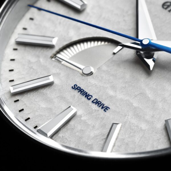 Nahaufnahme der Grand Seiko Heritage Spring Drive SBGA211 Armbanduhr mit strukturiertem silbernem Zifferblatt, eleganten silbernen Stundenmarkierungen und blauem Sekundenzeiger. „Spring Drive“ ist unten zu sehen. Oben links befindet sich eine kleine Gangreserveanzeige.