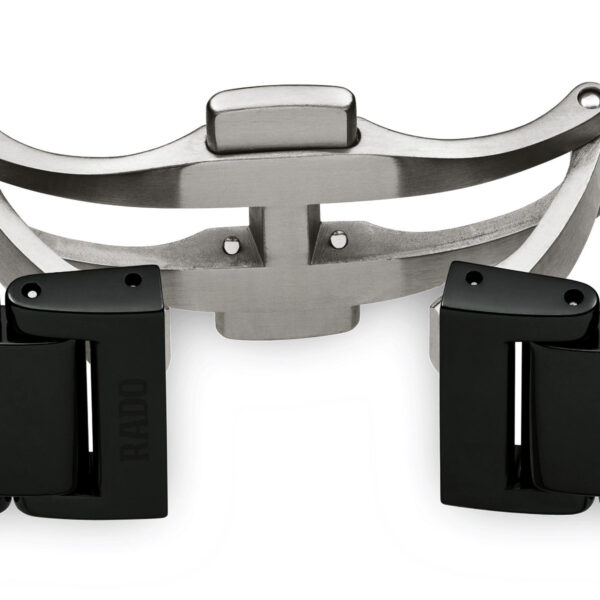 Eine Nahaufnahme des Verschlusses einer Rado True Automatic-Uhr zeigt ihr silbernes Design mit zwei schwarzen Keramikgliedern, einer gebogenen Form und einem teilweise offenen Mechanismus, wobei auf einem Glied „Rado“ sichtbar ist.