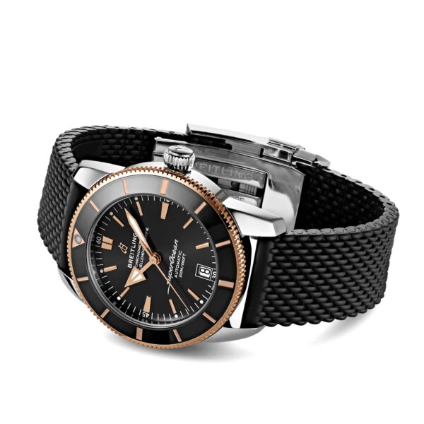 Die Breitling Superocean Heritage II B20 42 ist eine Luxusuhr mit schwarzem Zifferblatt, roségoldenen und weißen Stundenmarkierungen, eingefasst in Silber mit roségoldener Lünette. Sie verfügt über ein Edelstahlgehäuse, ein schwarzes Mesh-Armband und eine markante Aufzugskrone.