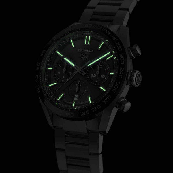 Die TAG Heuer Carrera Calibre Heuer 02 ist eine elegante schwarze Armbanduhr im Chronographen-Design mit leuchtenden Zeigern und Markierungen, die vor dunklem Hintergrund grün leuchten. Das Metallarmband und die detailreiche Lünette verleihen ihr einen modernen, eleganten Look.