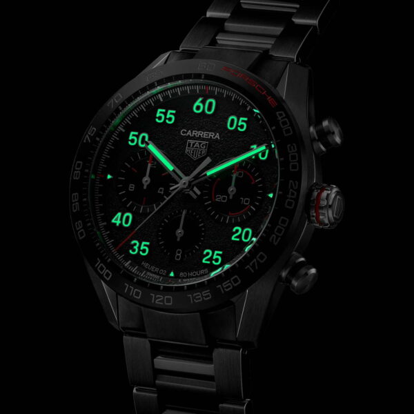 Eine Nahaufnahme der TAG Heuer Carrera Porsche Chronographen-Armbanduhr mit leuchtend grünen Ziffern und Markierungen, mehreren Hilfszifferblättern und einem zentralen Logo. Die Lünette und das Metallarmband unterstreichen ihre Eleganz vor dunklem Hintergrund.
