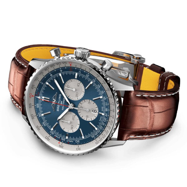 Die Breitling Navitimer B01 Chronograph 46 ist eine Luxusarmbanduhr mit blauem Zifferblatt, braunem Lederarmband und gelber Innenseite. Sie verfügt über drei Hilfszifferblätter, eine Datumsanzeige, ein silbernes Gehäuse mit strukturierter Lünette und weißen Markierungen.