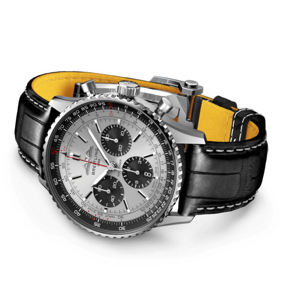 Die Breitling Navitimer B01 Chronograph 43 ist eine silberne Uhr mit schwarzem Lederarmband. Sie besticht durch ein weißes Zifferblatt mit Hilfszifferblättern und roten Akzenten auf der kreisförmigen Skala. Das gelbe Armband an der Innenseite unterstreicht das stilvolle Design.