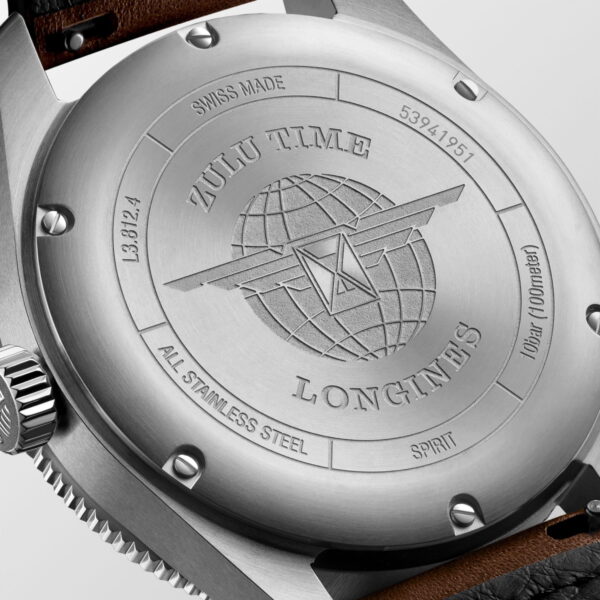 Nahaufnahme des Edelstahlgehäuses der Uhr Longines Spirit Zulu Time mit eingravierten Texten wie „Zulu Time“ und „Longines“, einem Globus mit einem Flugzeug, dekorativen Linien und technischen Details am Rand.