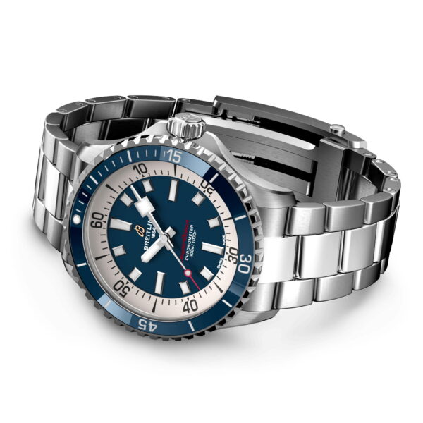 Die Breitling Superocean III Automatic 42, eine Edelstahlarmbanduhr mit blau-silbernem Zifferblatt, besticht durch weiße Stundenmarkierungen und Zeiger. Die Lünette verfügt über Minutenmarkierungen und ein poliertes Armband, das schräg auf einer glatten Oberfläche liegt.
