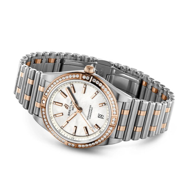Die Breitling Chronomat Automatic 36 ist eine Luxusuhr mit weißem Zifferblatt, goldenen Stundenmarkierungen, Datumsanzeige und Markenlogo. Sie verfügt über eine diamantbesetzte Lünette und ein Armband aus abwechselnd silbernen und goldenen Gliedern.