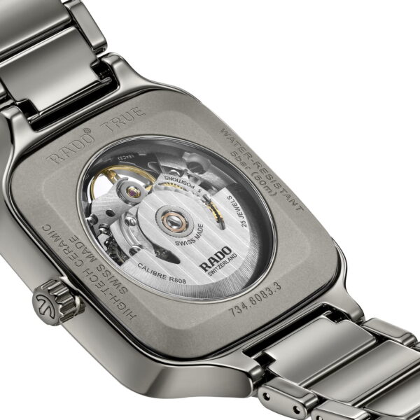 Eine Nahaufnahme der True Square Automatic Skeleton Armbanduhr offenbart ihr mechanisches Uhrwerk durch ein transparentes Gehäuse mit filigranen Zahnrädern. Auf der silbernen Metallrückseite sind Marken- und Modellangaben eingraviert.