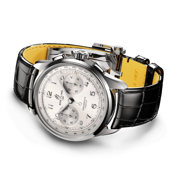 Der Breitling Premier B09 Chronograph ist eine silberne Uhr mit weißem Zifferblatt, drei Hilfszifferblättern und markanten Ziffern. Sie verfügt über ein schwarzes Lederarmband mit gelbem Futter und ein Edelstahlgehäuse, das seitlich mit teilweise geöffnetem Armband präsentiert wird.